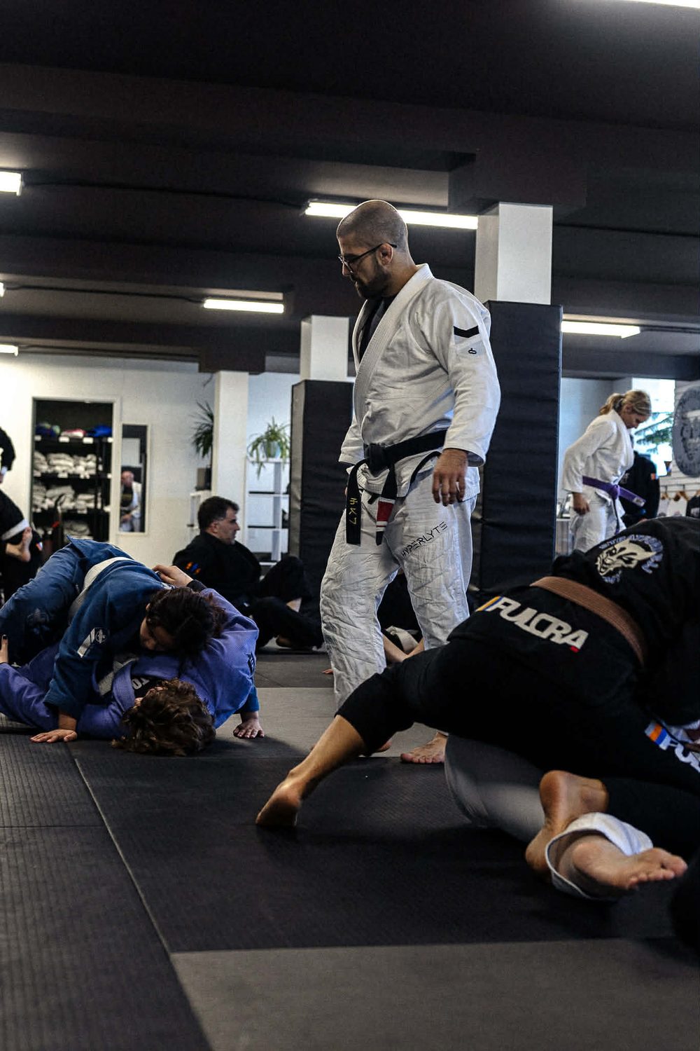 A coach reading the room while pairs of adults roll during live training