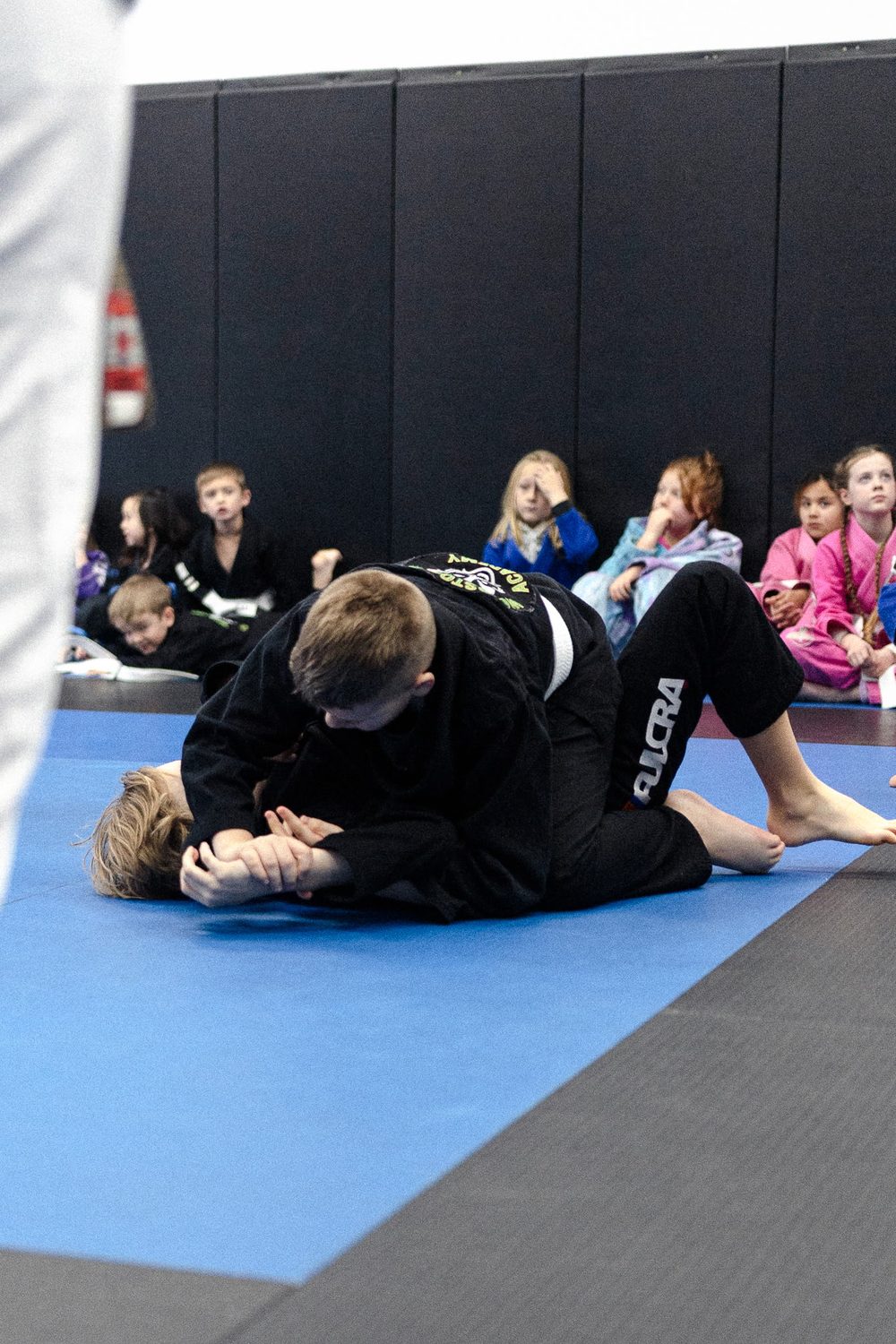 Kids class in progress, a coach coaching a pair through a drill while the rest watch